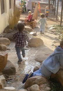 children running in water and boulders away from the camera